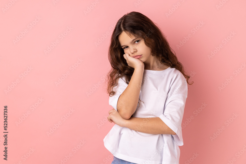 Portrait of lazy bored little girl wearing white T-shirt leaning on hand and looking depressed, child with indifferent gloomy expression has no energy. Indoor studio shot isolated on pink background. Portrait of lazy bored little girl wearing white T-shirt leaning on hand and looking depressed, child with indifferent gloomy expression has no energy. Indoor studio shot isolated on pink background.