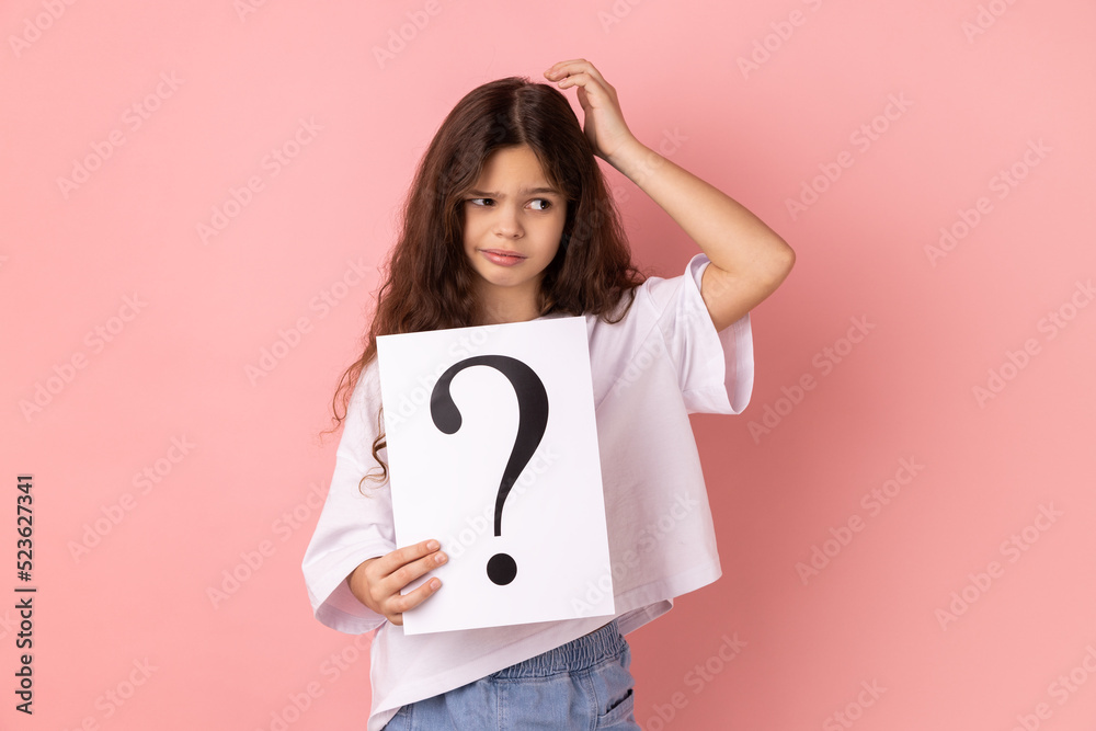 Portrait of little girl wearing white T-shirt holding paper with question mark over, thoughtful, face thinking about question, very confused idea. Indoor studio shot isolated on pink background. Portrait of little girl wearing white T-shirt holding paper with question mark over, thoughtful, face thinking about question, very confused idea. Indoor studio shot isolated on pink background.
