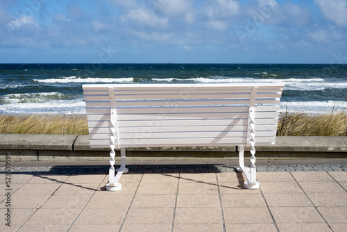 Fototapeta Naklejka Na Ścianę i Meble -  White bench on the promenade at the Baltic Sea in the sunshine