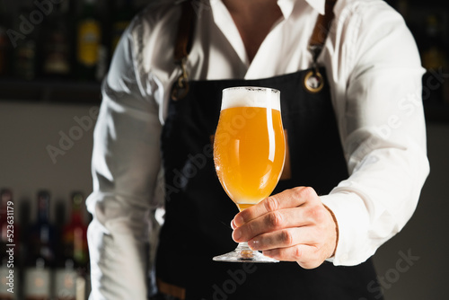 Beer. A professional bartender in a white shirt and black apron holds a glass of beer, the trend drinks concept.