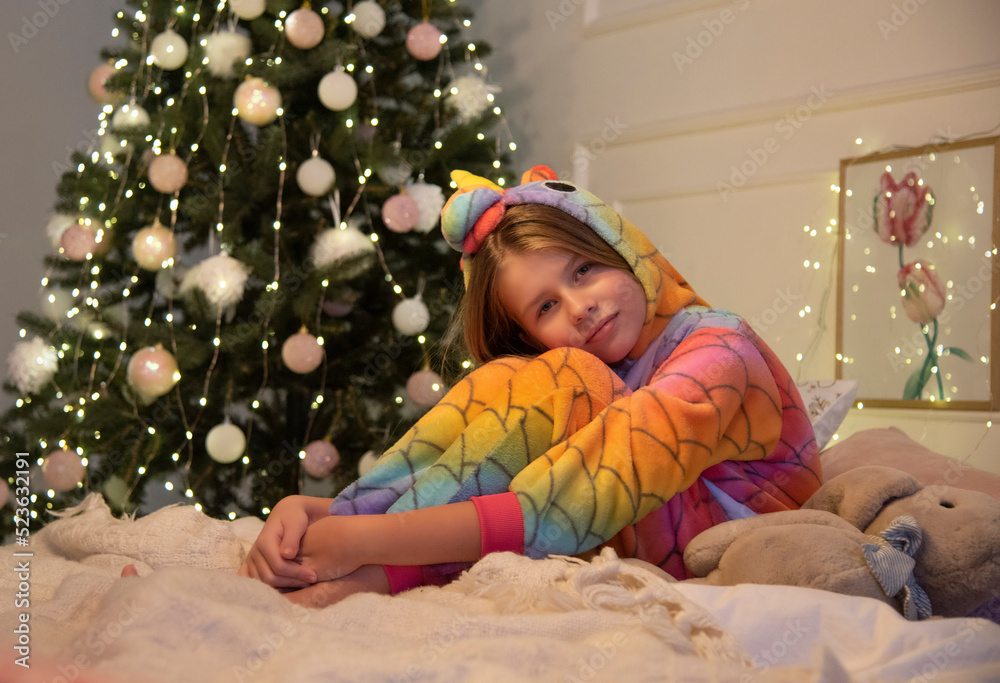 beautiful girl in pajamas with a unicorn sitting near the Christmas tree in bedroom with night lights beautiful girl in pajamas with a unicorn sitting near the Christmas tree in bedroom with night lights