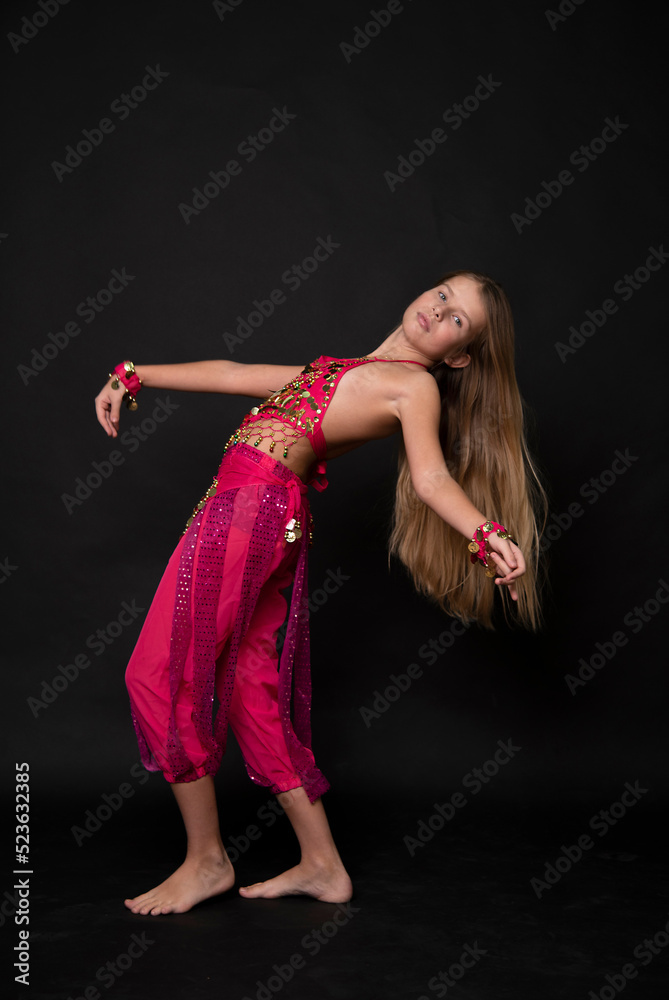 a young beautiful blonde girl in a pink outfit dances an oriental belly dance on black background