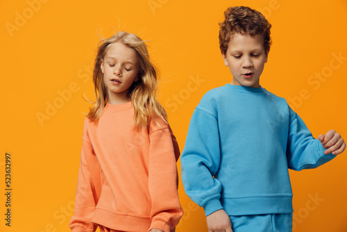 cute, beautiful children, brother and sister stand on a yellow background in bright clothes with their eyes closed, dynamically posing