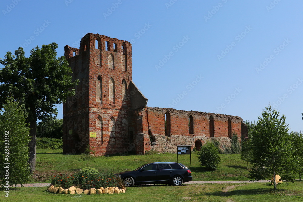Ruiny kościoła gotyckiego z czerwonej cegły i stojący przed nim czarny samochód - obrazy, fototapety, plakaty 