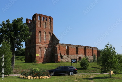 Ruiny kościoła gotyckiego z czerwonej cegły i stojący przed nim czarny samochód