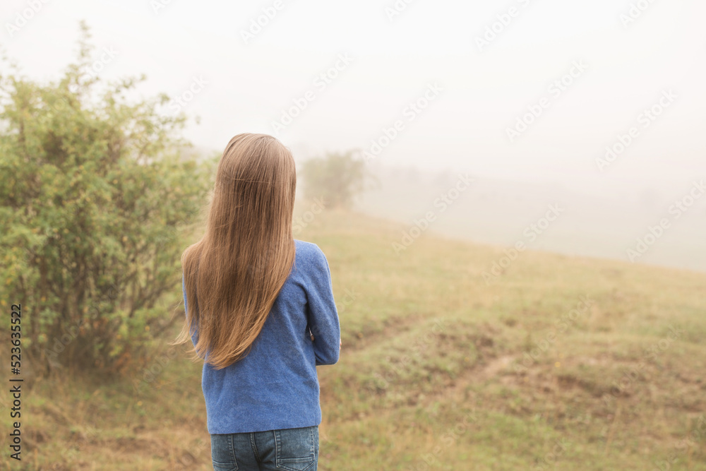 Long-haired girl walking on a foggy morning, back view Long-haired girl walking on a foggy morning, back view