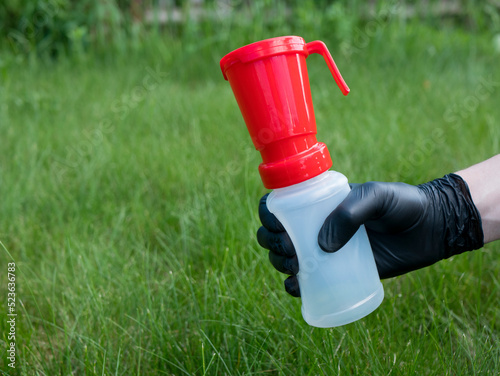 Hand in black nitrile glove holding a teat dip cup for udder cow disinfection on green grass background, copy space. Milking practice