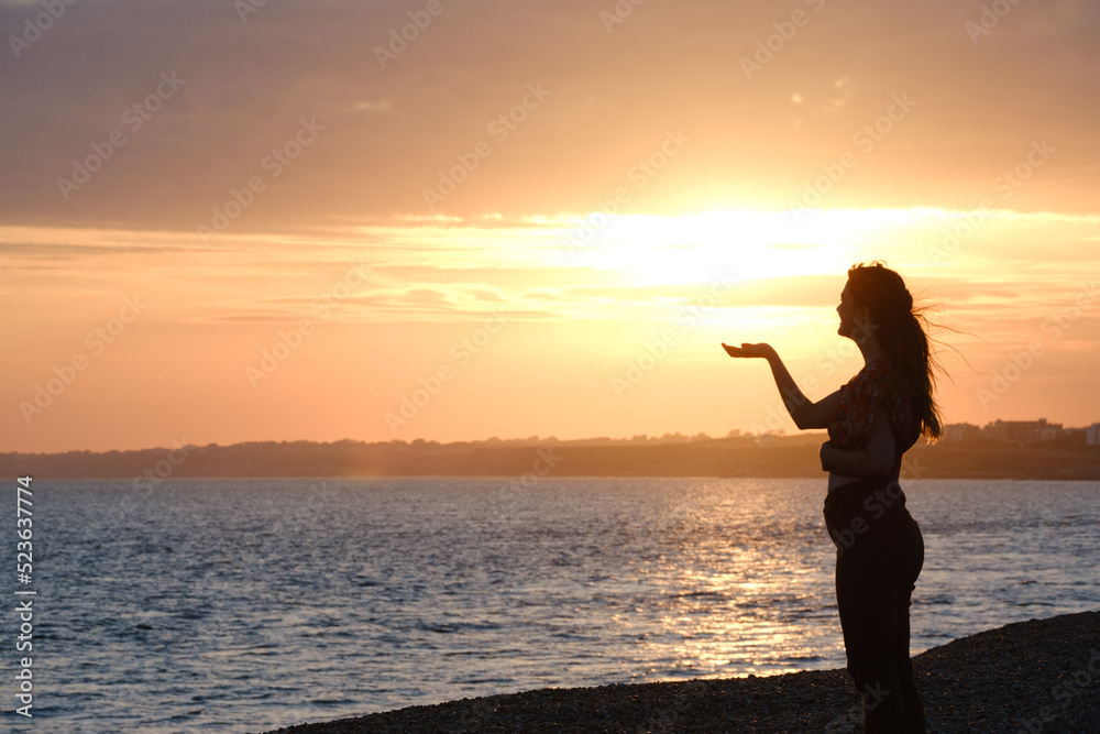 Fototapeta premium silhouette of a woman on the beach holding the sunset