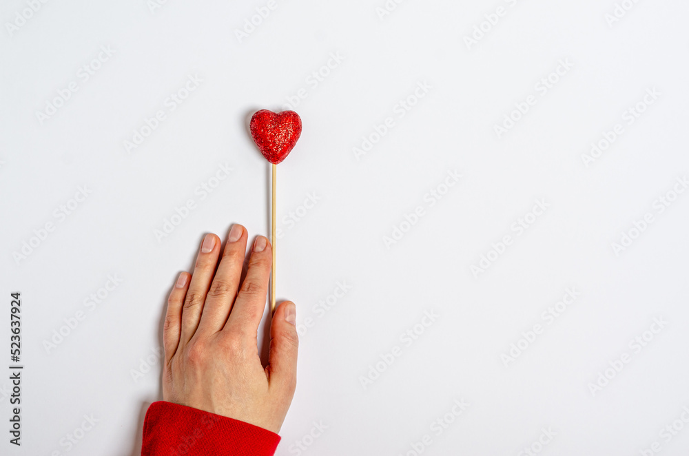Shiny heart on a stick in a female hand on a white background