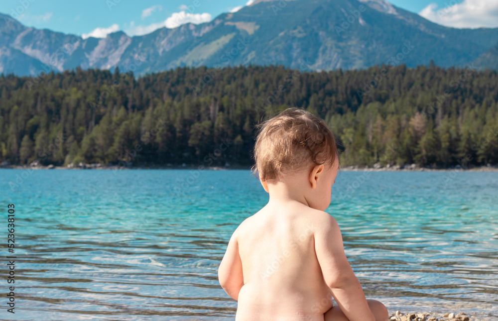 naked adorable baby boy sitting with back on scenic beautiful mountains lake landscape background playing in water.rocks pebbles beach turquoise blue clean water.sunny summer day,light.kid having fun naked adorable baby boy sitting with back on scenic beautiful mountains lake landscape background playing in water.rocks pebbles beach turquoise blue clean water.sunny summer day,light.kid having fun