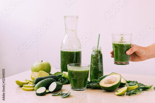 Female hand holding glass with green vegetable fruit smoothie drink light background. Vegetarianism