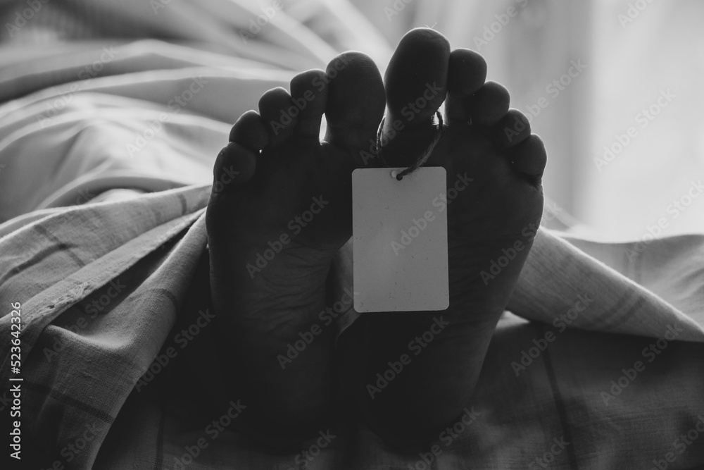 Φωτογραφία Women's legs with a tag covered with a sheet on the table, the legs of a dead pe