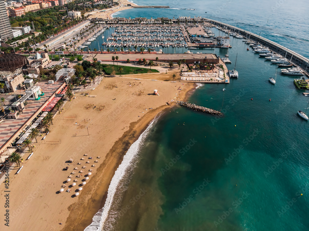 Drone shot Barcelona. Port with boats near the coast. Drone view of a vibrant swimming and sunbathing beach in Barcelona. People are relaxing on the beach. Panoramic view of the city of Barcelona.
