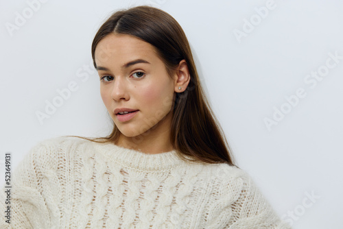 a beautiful, attractive woman in a white autumn, warm sweater stands on a light background looking pleasantly into the camera and smiling gently