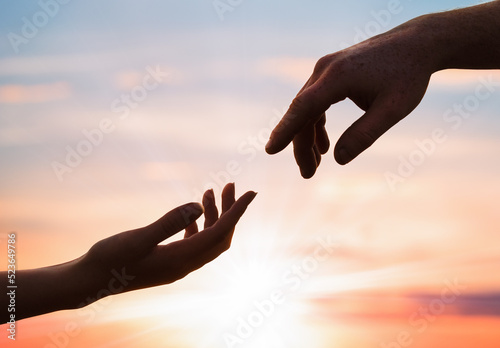 silhouettes of a female and male hand reaching out to each other against the background of a sunset