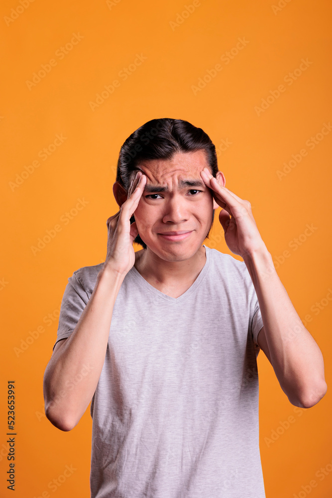 Asian man suffering from headache, touching temples with fingers, looking at camera. Exhausted teenager having migraine, overworked stressed young person feeling unwell, mid shot Asian man suffering from headache, touching temples with fingers, looking at camera. Exhausted teenager having migraine, overworked stressed young person feeling unwell, mid shot