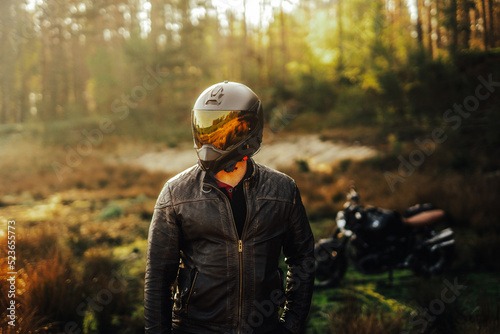 biker with a black helmet walking away from his motorcycle at sunrise