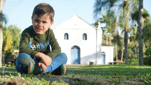 Menino sentado em um gramado em frente a uma igrja do interior photo