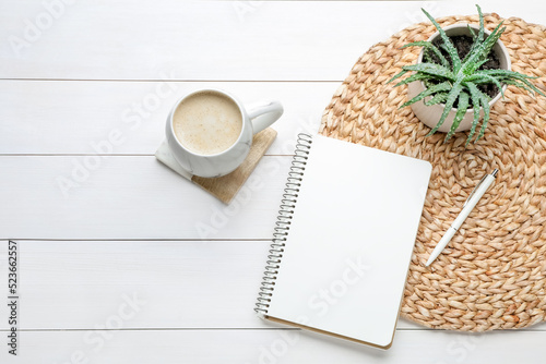 Mug of coffee with stylish cup coaster, houseplant and notebook on white wooden table, flat lay. Space for text