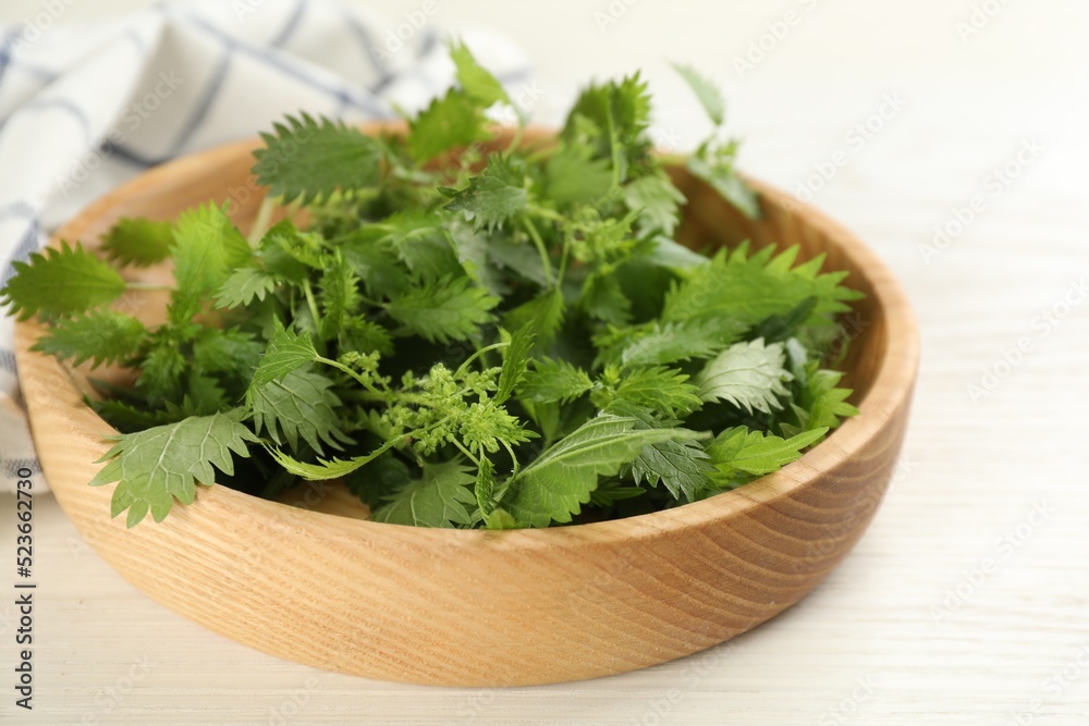 Wooden plate with fresh stinging nettle leaves on white table, closeup Wooden plate with fresh stinging nettle leaves on white table, closeup