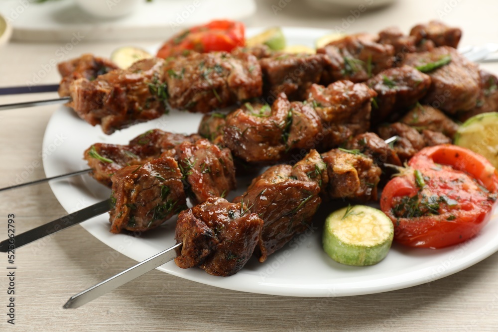 Metal skewers with delicious meat and vegetables served on white wooden table, closeup