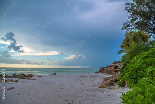 Siesta Key, Florida, popular travel tourist destination. Scene of the beach near Siesta Key Village at dusk as a storm appears in the distant sky. Cool blue turquois water along the rock studded shore