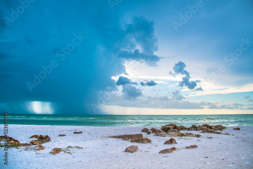 Siesta Key, Florida, popular travel tourist destination. Scene of the beach near Siesta Key Village at dusk as a storm appears in the distant sky. Cool blue turquois water along the rock studded shore
