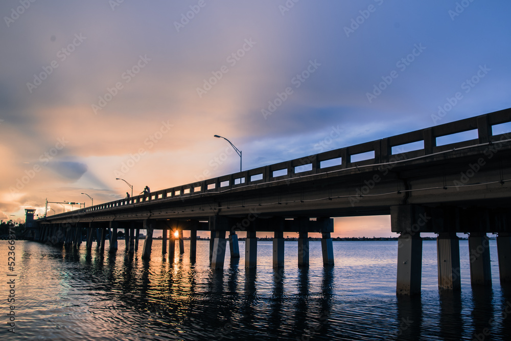 Fototapeta premium View of Sarasota Bay near Siesta Key Beach at sunset with view of road bridge disappearing into the distance. Colorful sky at dusk over the water. 