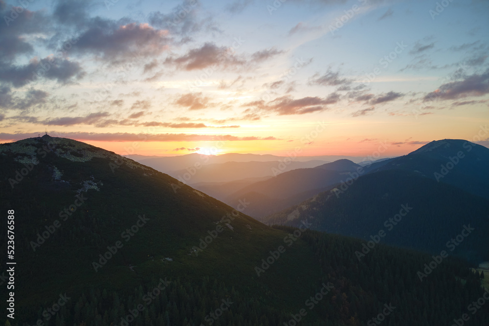 Aerial view of amazing scenery with foggy dark mountain peak covered with forest pine trees at autumn sunrise. Beautiful wild woodland with shining rays of light at dawn