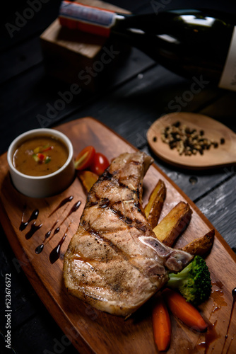 grilled pork steak on wooden plate on black background