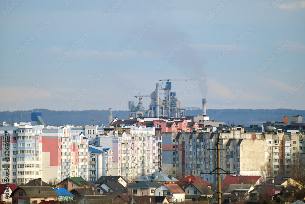 Cement plant with high factory structure and tower cranes at industrial production area near city urban area. Manufacture and global industry concept