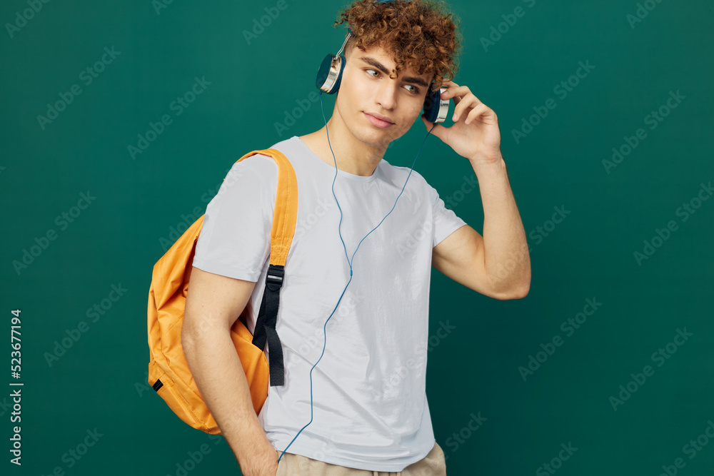horizontal portrait of a handsome man, a student, with curly hair, standing on a green background in a gray T-shirt, and straightens headphones with his hand horizontal portrait of a handsome man, a student, with curly hair, standing on a green background in a gray T-shirt, and straightens headphones with his hand
