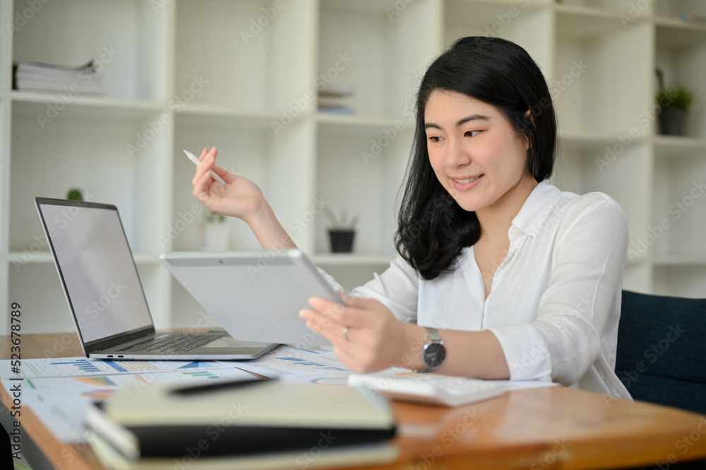 Asian businesswoman working in the office, using digital tablet and laptop.