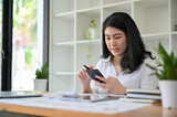 Attractive young Asian businesswoman at her office desk using her smartphone.