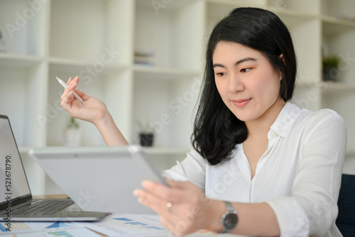 Professional Asian businesswoman is using and looking at a digital tablet at her office desk.