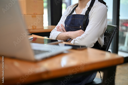 Asian female entrepreneur sits at her office desk with arms crossed. cropped image