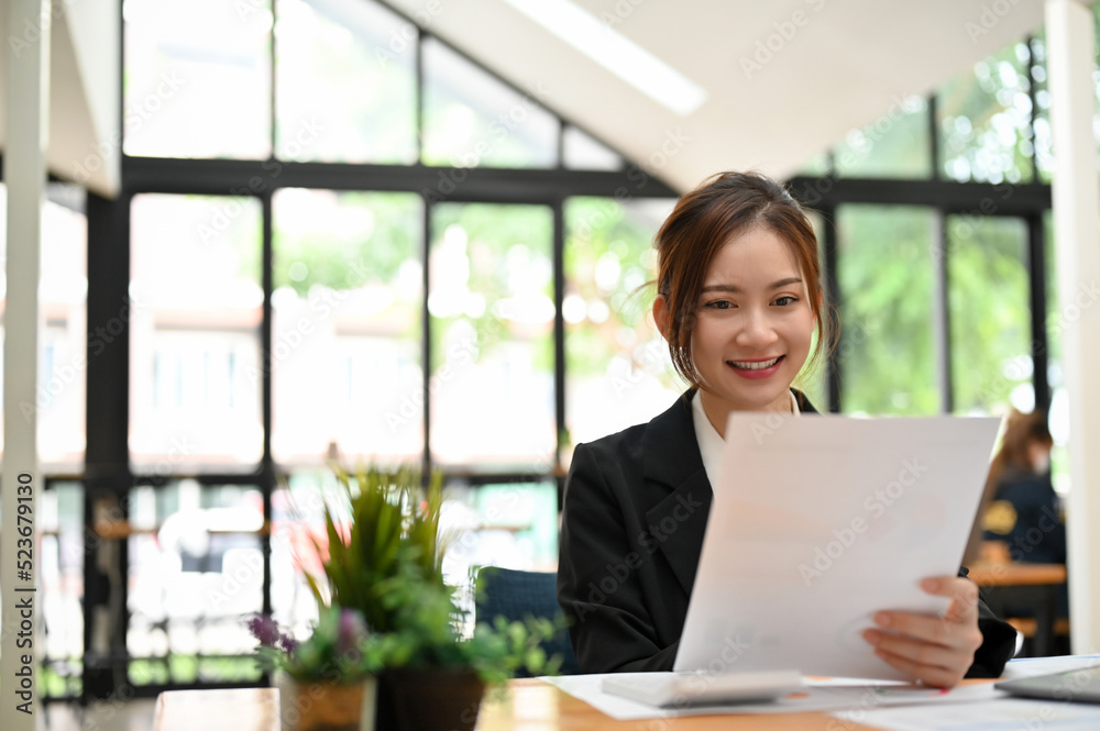 Beautiful young Asian female office worker reading business information on paper Beautiful young Asian female office worker reading business information on paper