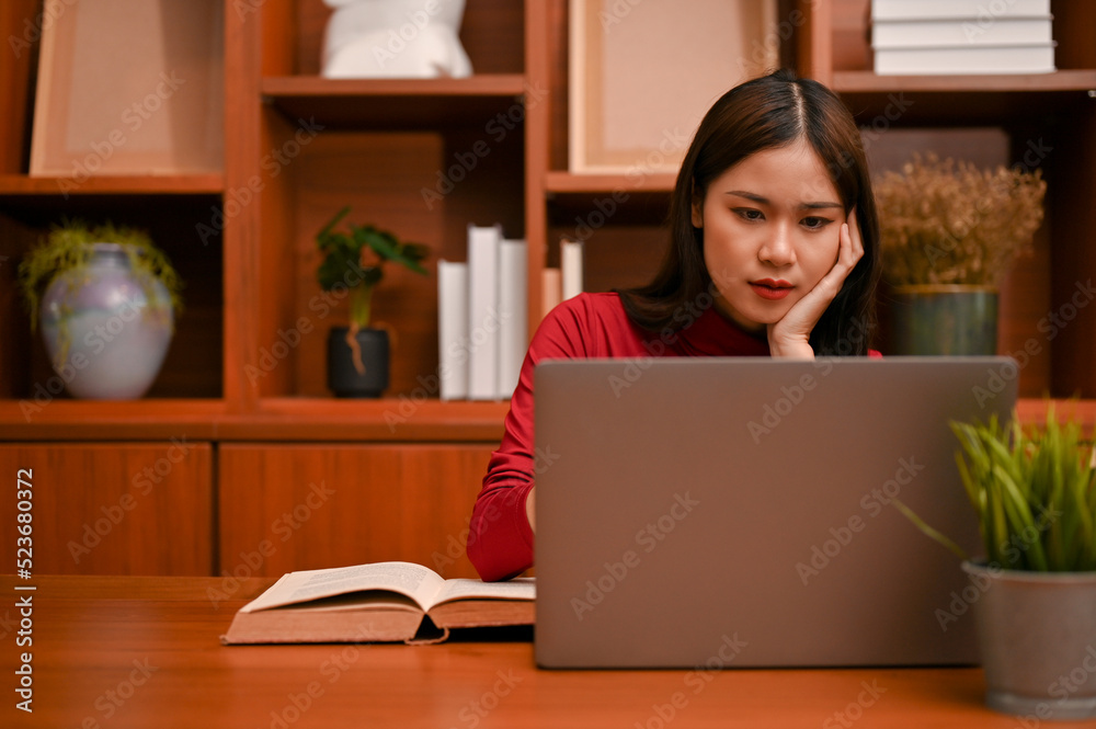 Asian businesswoman working on her laptop, thinking pensively and planning her project Asian businesswoman working on her laptop, thinking pensively and planning her project