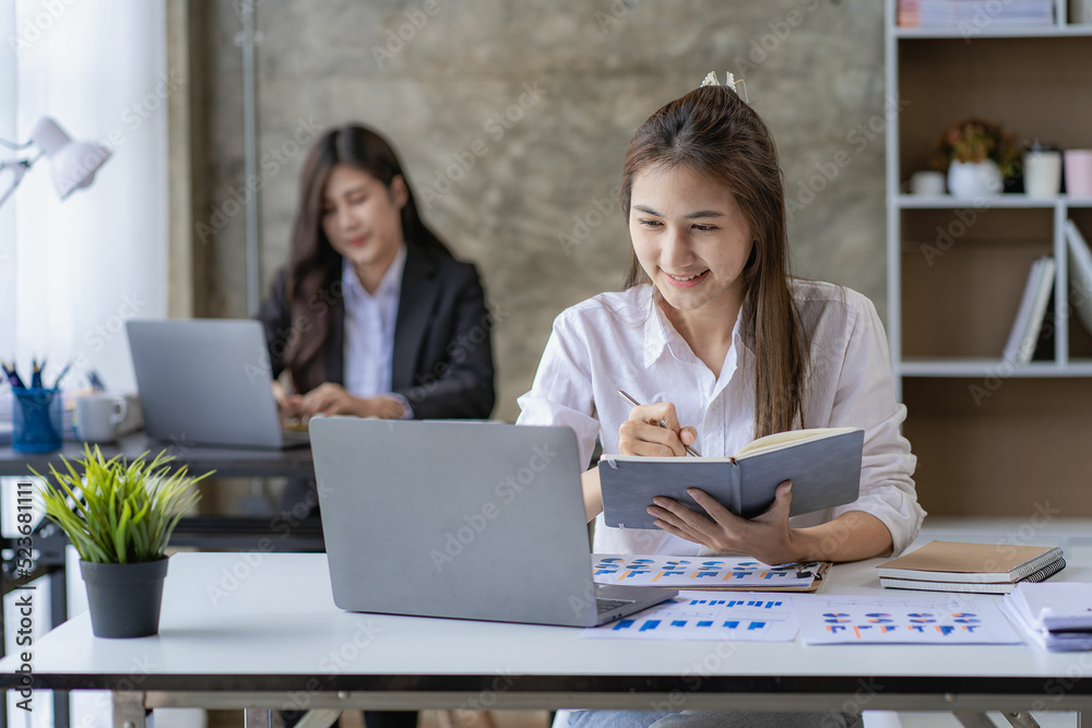 Two Asian women with laptop and financial graphs calculating accounting and taxes at the office. business idea Two Asian women with laptop and financial graphs calculating accounting and taxes at the office. business idea