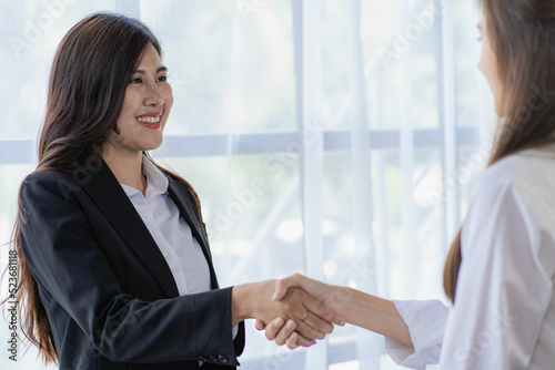 Two young Asian business women shake hands with their coworkers in a meeting, looking at each other. © ArLawKa