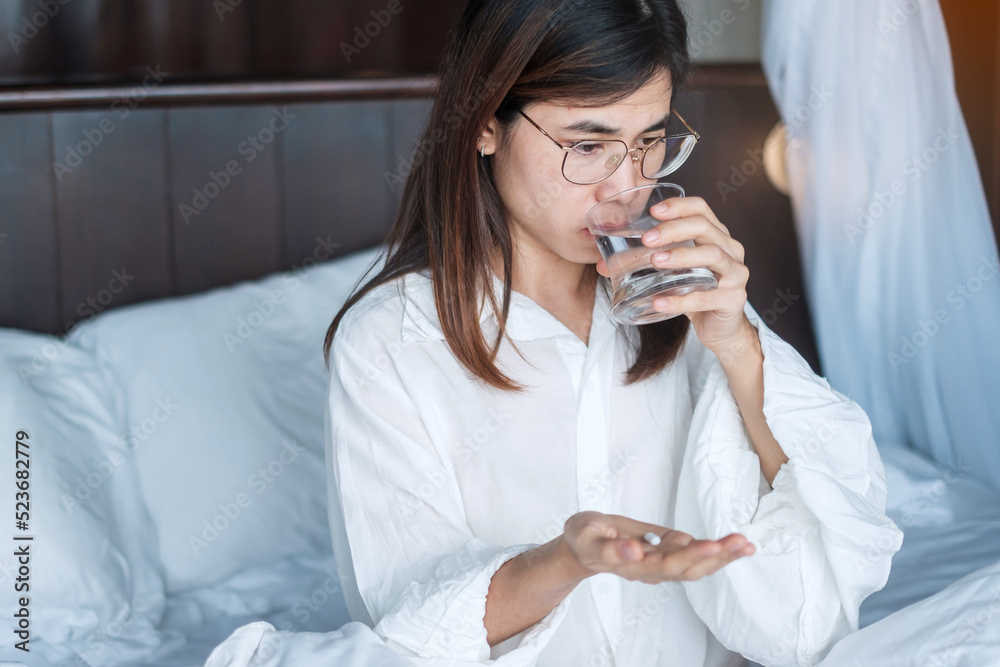 woman drinking water during taking medicine pill on bed at home. Drug, Migraine, painkiller, headache, influenza, illness, sickness and healthcare concept woman drinking water during taking medicine pill on bed at home. Drug, Migraine, painkiller, headache, influenza, illness, sickness and healthcare concept