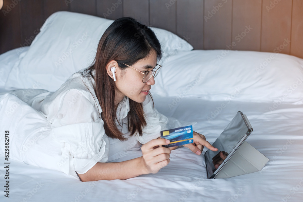 woman using tablet and credit card for online shopping while making order on bed in morning at home. technology, ecommerce, digital banking online payment and apartment living concept