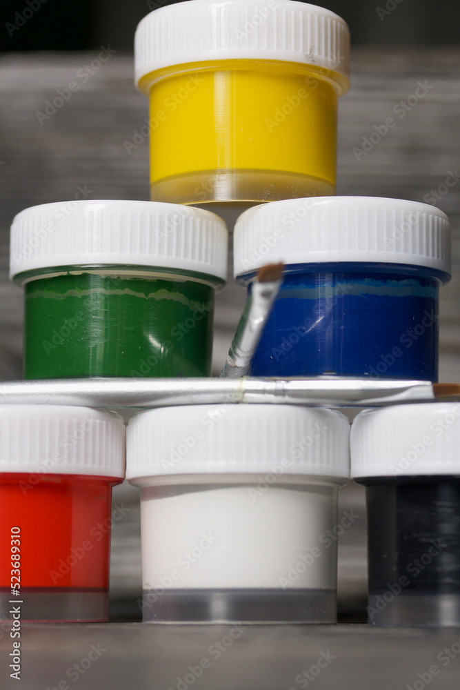 A set of gouache and brushes for drawing. Jars of paint stand in a pyramid. On pine boards. Close-up. A set of gouache and brushes for drawing. Jars of paint stand in a pyramid. On pine boards. Close-up.