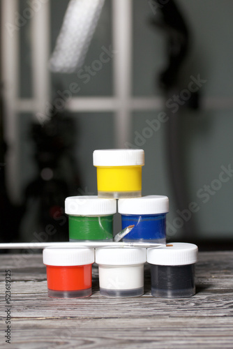 A set of gouache and brushes for drawing.  Jars of paint stand in a pyramid.  On pine boards.
