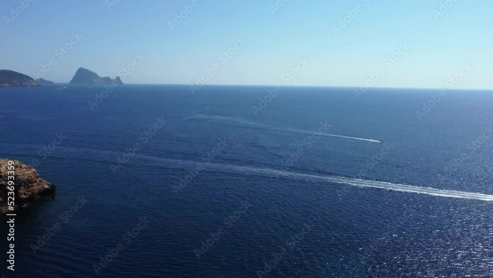 Motor boats, stony small islands in seaSpectacular aerial view flight pan 180 overview drone footageof cliff edge beach Sa Figuera borda Ibiza summer 2022.