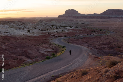 Woman walking on Scenic Road in the Desert at Sunrise with Red Rock Mountain Landscape. Spring Season. Goblin Valley State Park. Utah, United States. Nature Background.