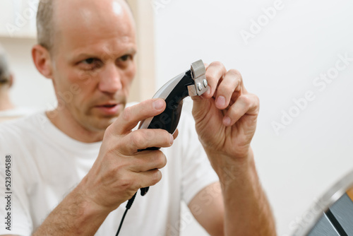 Adult guy using shaving machine trimmer to cut his hair at gome