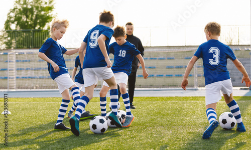 Fototapeta Naklejka Na Ścianę i Meble -  Happy Kids on Training Soccer Drill. Young European Footballers Dribbling Balls. Soccer Boys in Training With School Young Coach