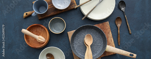 Set of kitchen utensils and dinnerware on dark background, top view