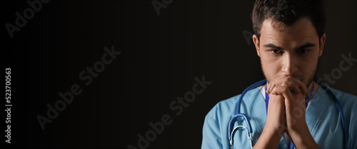 Praying male doctor on dark...